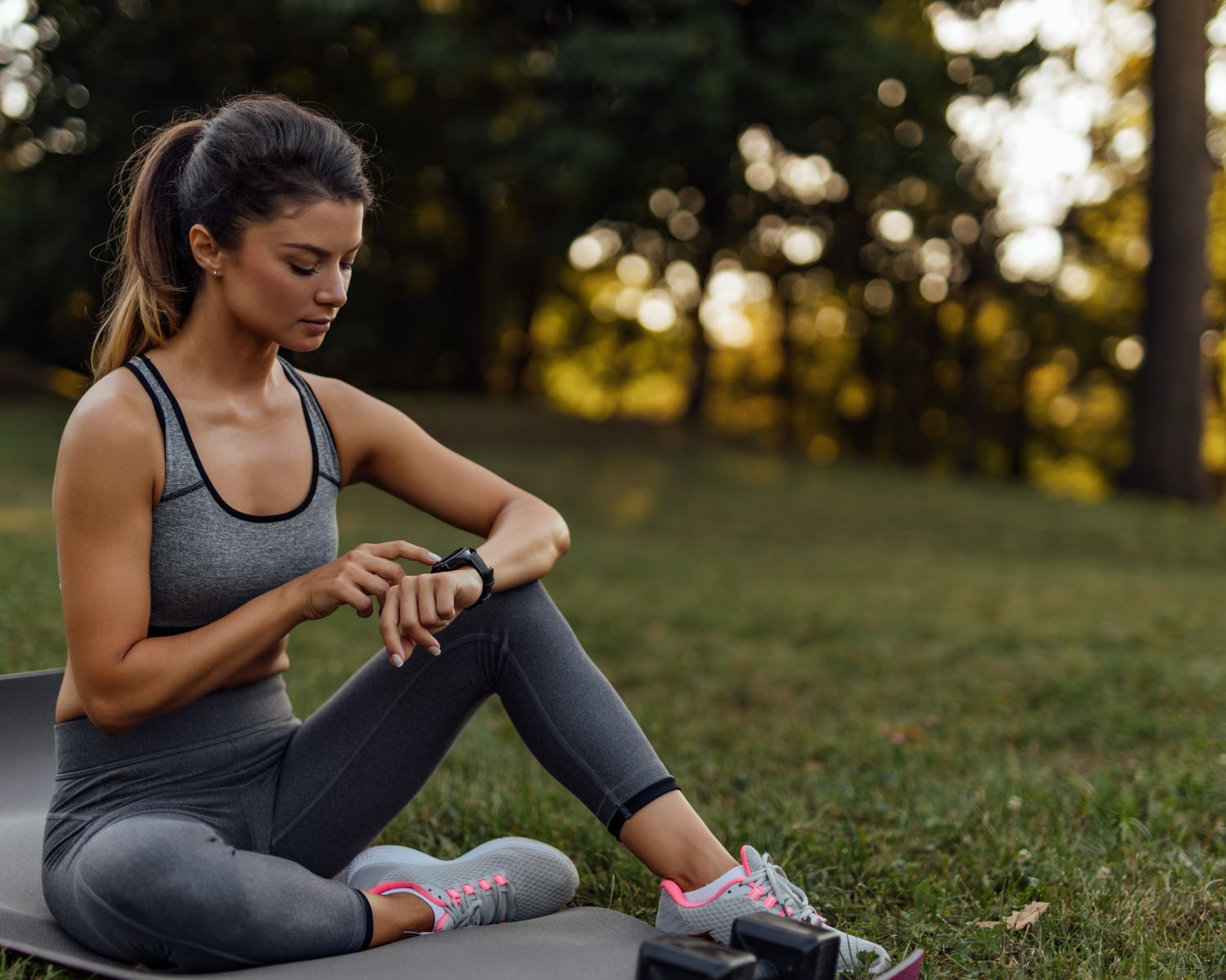 Jeune femme assise sur un tapis de sport, consultant sa montre digitale