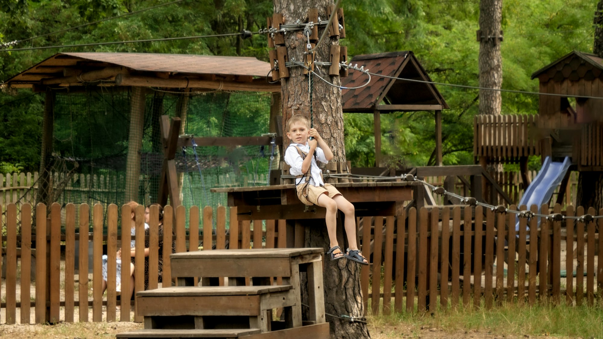 Portrait of happy cheerful boy riding on the zip line at extreme adventure park. Kids sports